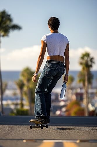 Personne faisant du skateboard sur une route, tenant une bouteille d'eau.